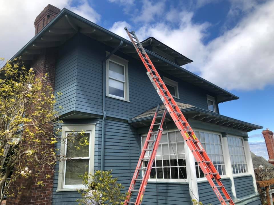 Exterior painting in progress on a blue Craftsman-style house